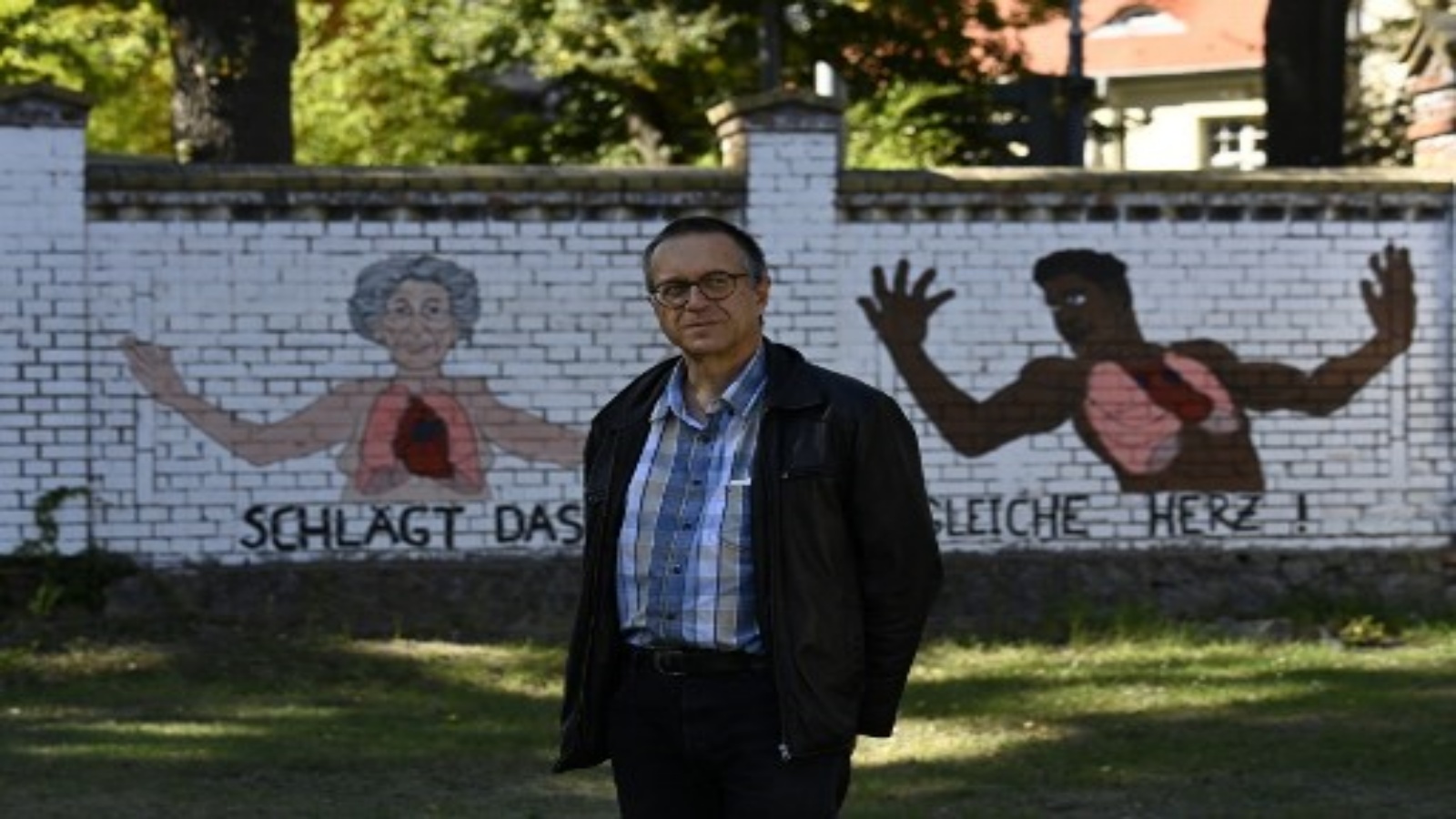 مارتن أوسينسكي في حديقة عامة مع كتابات على الجدار الخلفي كتب عليه 
