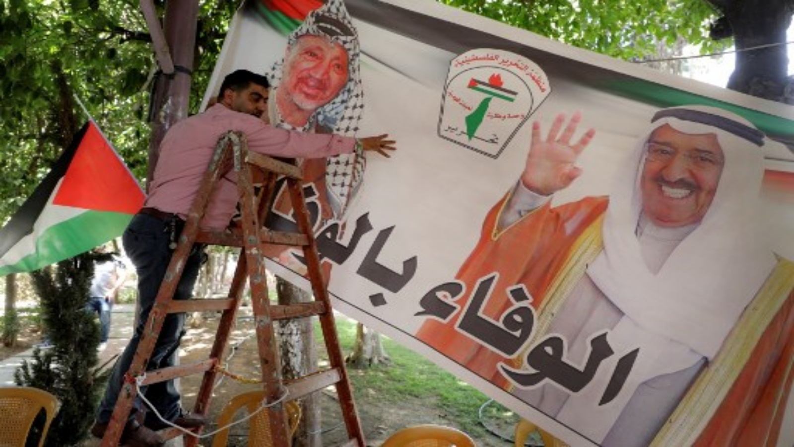 فلسطينيون يعلقون لافتة عليها صور أمير الكويت الراحل الشيخ صباح الأحمد الصباح (إلى اليمين) والزعيم الفلسطيني الراحل ياسر عرفات في مدينة نابلس بالضفة الغربية، 30 سبتمبر 2020. أ ف ب