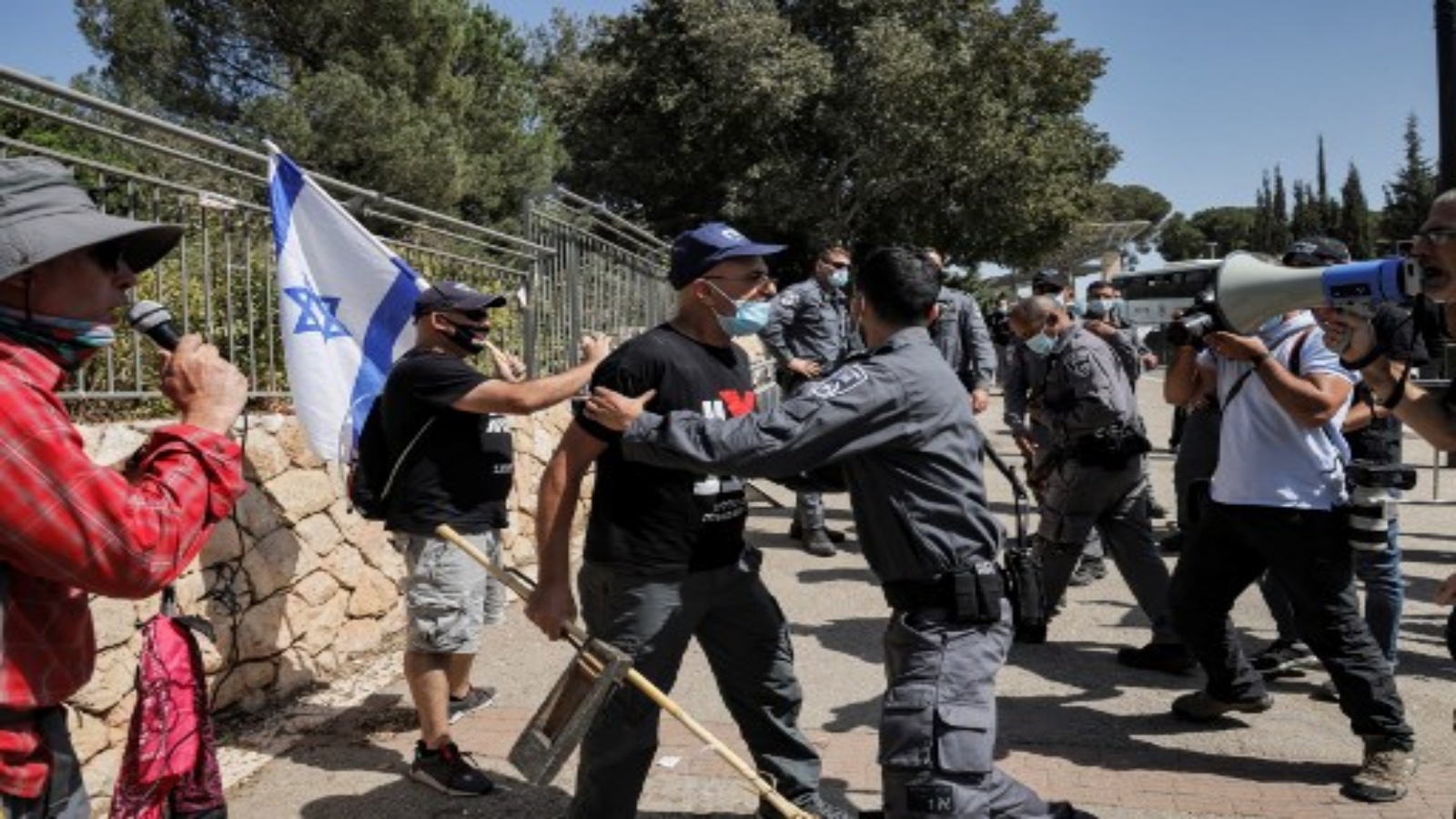 شرطي إسرائيلي يقف حاملا متظاهرا يواجهه ، كلهم ​​يرتدون أقنعة بسبب جائحة فيروس كورونا COVID-19 ، خلال مظاهرة خارج الكنيست (البرلمان الإسرائيلي) في القدس في 29 سبتمبر 2020 ، ضد مشروع قانون محتمل يقيد الاحتجاجات وسط جائحة جديد اللوائح