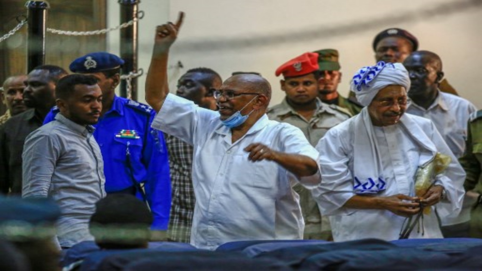 الرئيس السوداني المخلوع عمر البشير (وسط) يلوح له أثناء وصوله لمحاكمته في العاصمة الخرطوم ، في 6 أكتوبر 2020 ، إلى جانب 27 متهمًا مشاركًا في الانقلاب العسكري عام 1989 الذي أوصله إلى السلطة