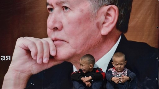 صبيان يجلسان على مقعد تحت لافتة انتخابية للحزب الديمقراطي الاجتماعي في قيرغيزستان تحمل صورة الرئيس القرغيزي السابق ألمازبيك أتامباييف في قرية أراشان، على بعد 20 كيلومترًا من بيشكيك. 30 سبتمبر 2020. 