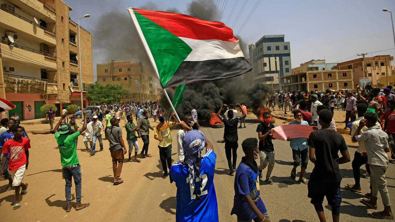 متظاهر سوداني يلوح بالعلم الوطني بينما يتصاعد الدخان من الإطارات المحترقة خلال مظاهرة شرق العاصمة الخرطوم في 30 حزيران/يونيو 2020