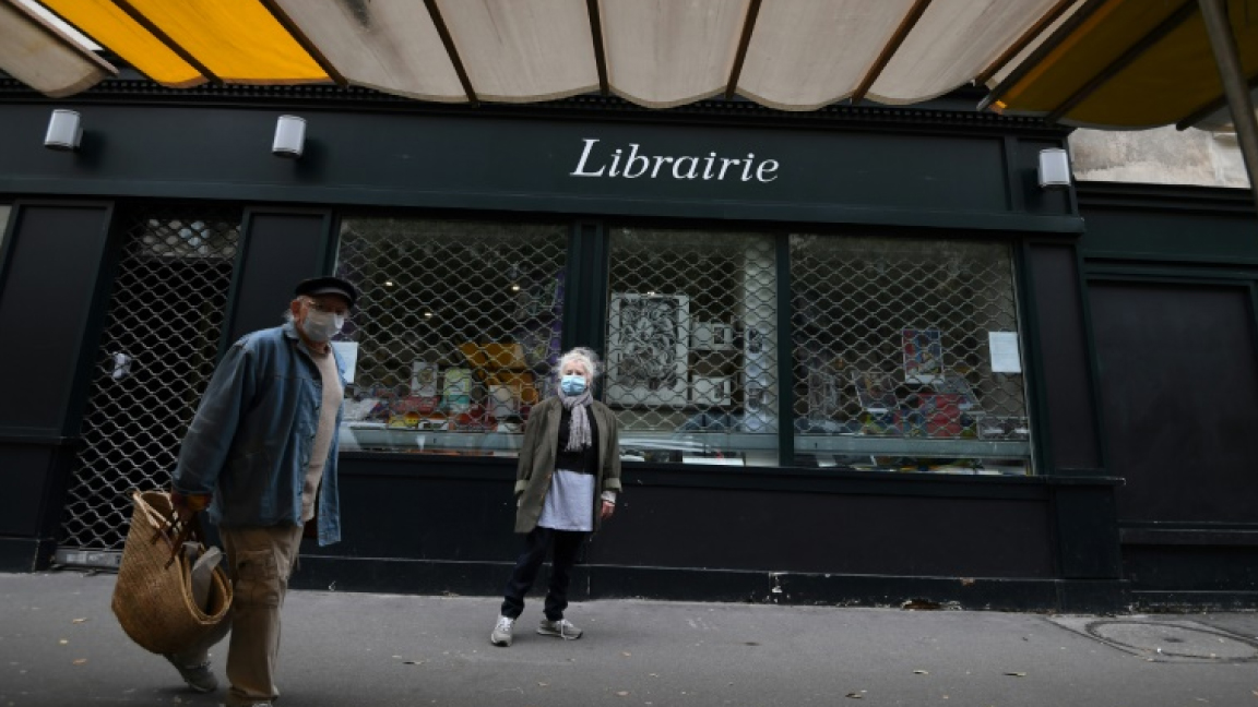 رجل وامرأة يعبران أمام متجر لبيع الكتب مقفل في باريس في أول ايام الإغلاق الجمعة