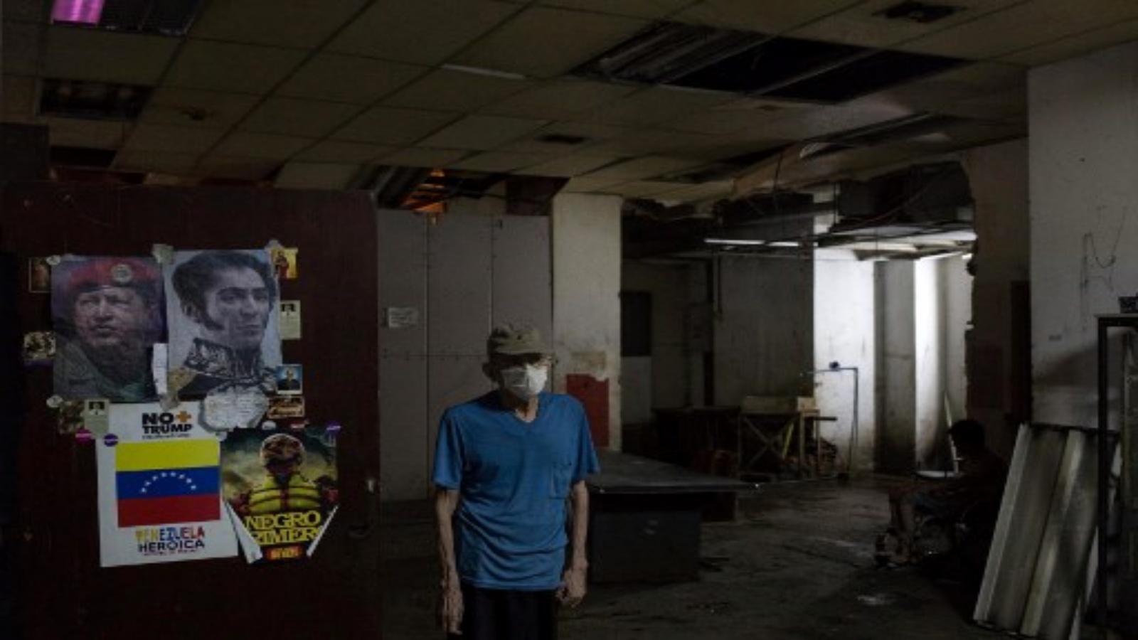 رجل يقف بجانب ملصقات تصور المحرر الفنزويلي سيمون بوليفار (يمين) والزعيم الفنزويلي الراحل هوغو تشافيز ، في قاعات ملجأ يقع في الطابق السفلي من مبنى Sudameris العام في كاراكاس ، في 9 أكتوبر 2020 ، وسط جائحة فيروس كورونا الجديد . تعيش 14 عائلة بدون كهرباء أو تهوية أو مياه جارية أو حمامات في الطابق السفلي من مبنى حكومي في كاراكاس مما يجعلها عرضة بشكل خاص لفيروس كورونا.