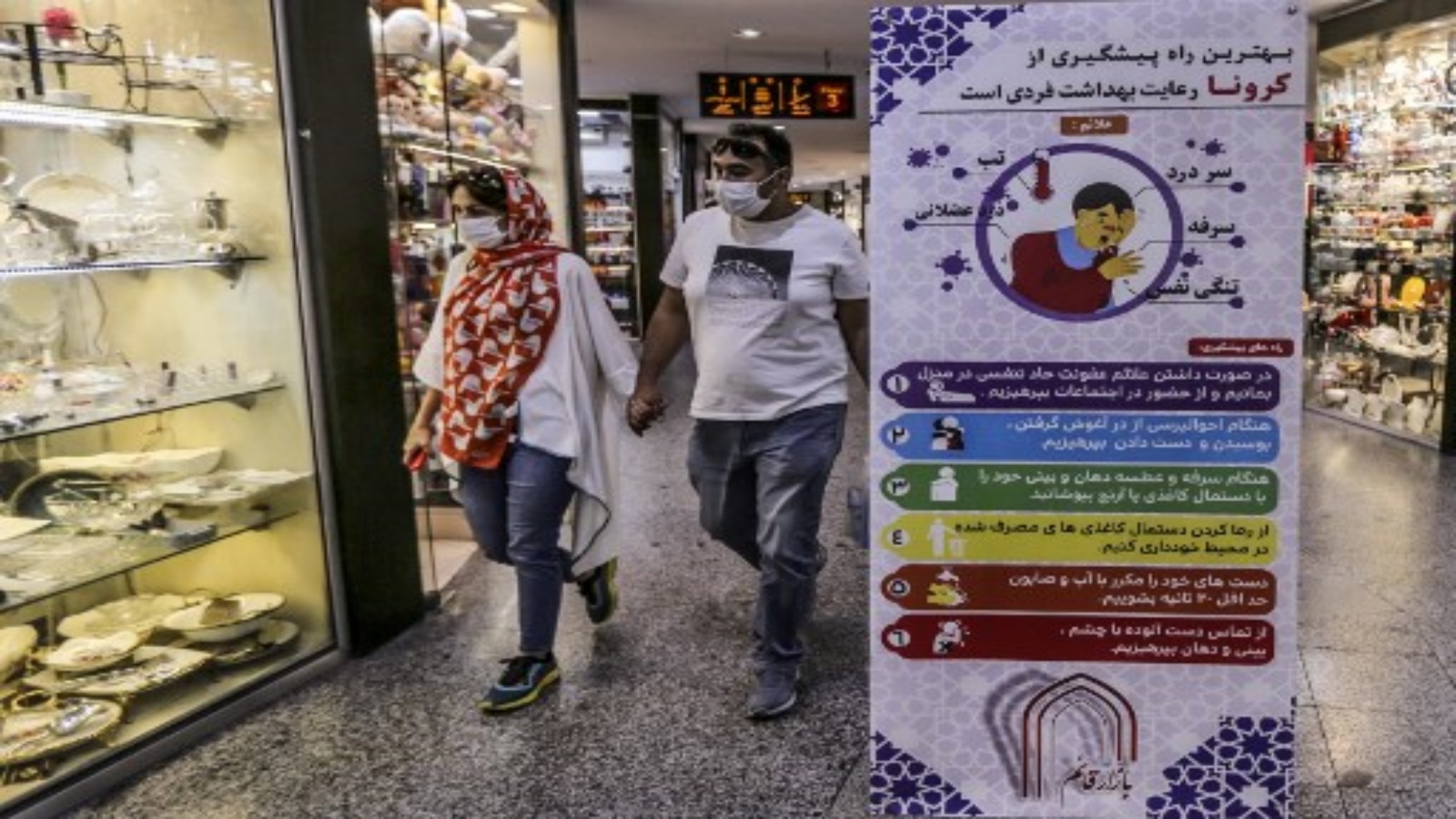 إيرانيان يمشيان بجوار لافتة تنصح الناس بارتداء أقنعة أثناء التسوق في ساحة تاجريش بالعاصمة طهران في 1 نوفمبر 2020 