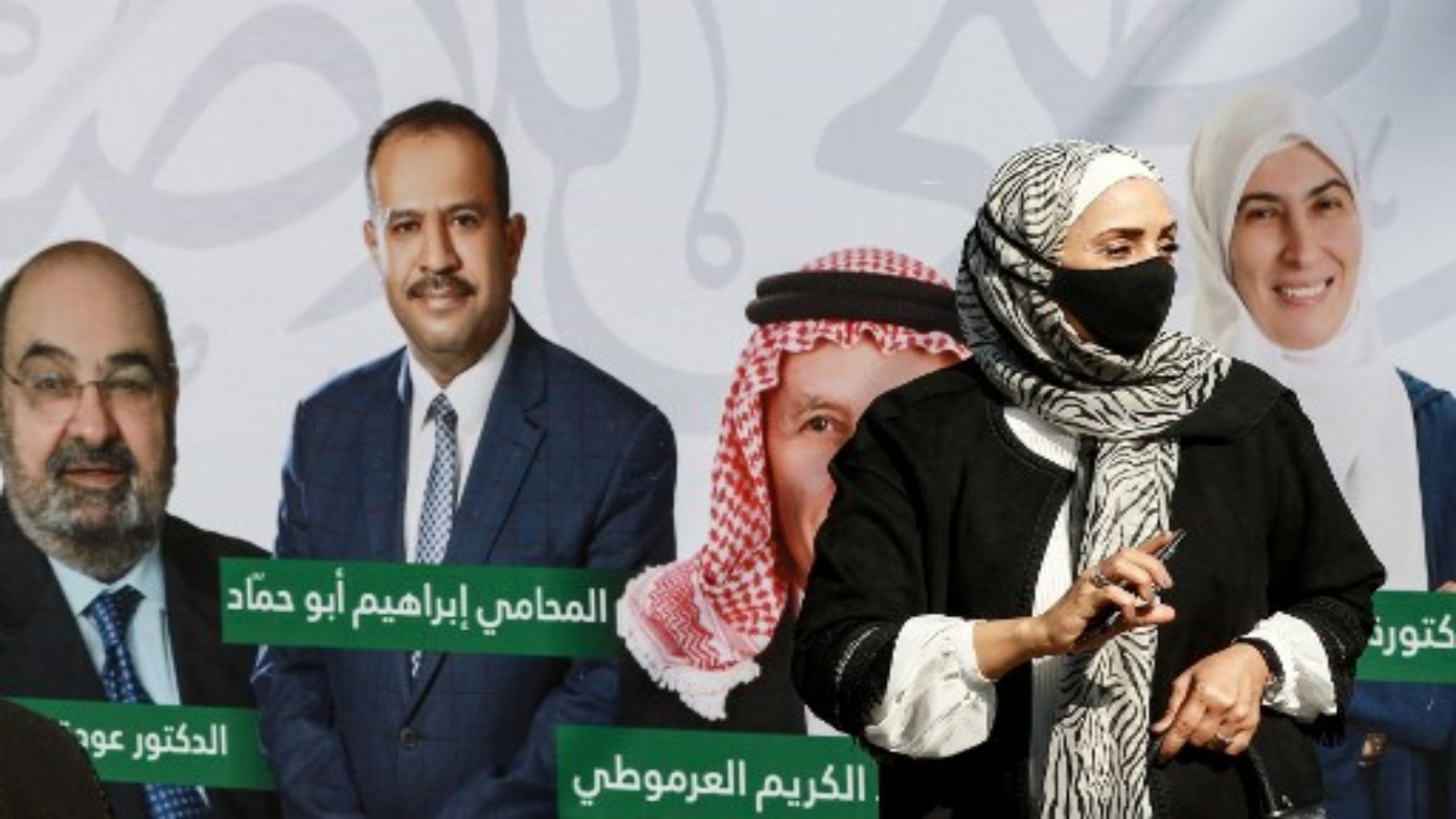 امرأة ترتدي أقنعة بسبب جائحة فيروس كورونا COVID-19 ، تقف بجانب ملصق حملة يظهر مرشحي قائمة انتخابية في العاصمة الأردنية عمان في 10 نوفمبر 2020 ، خلال الانتخابات العامة لعام 2020