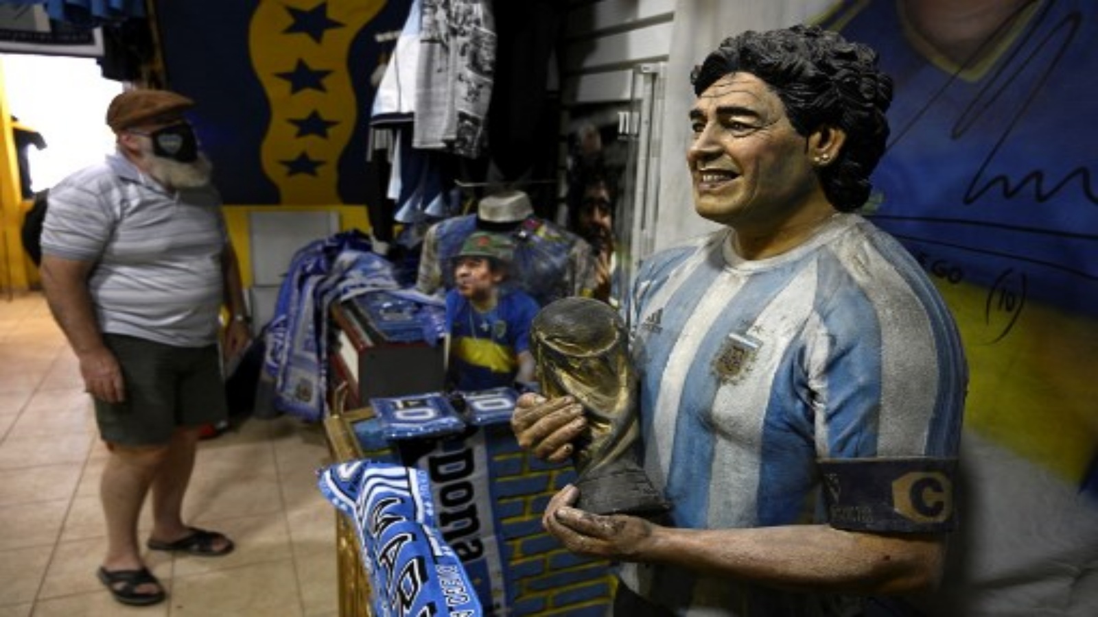  دمية تصور أسطورة كرة القدم الأرجنتينية الراحل دييجو مارادونا وهو يحمل كأس العالم FIFA محاطة بالترويج في متجر أمام استاد بوكا جونيورز 