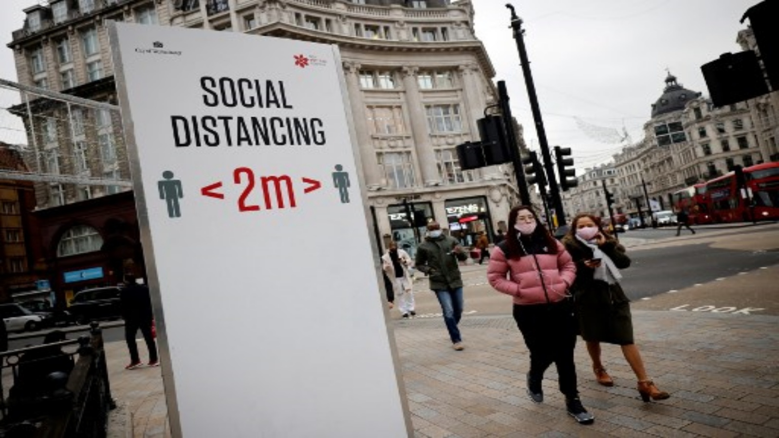 مشاة يمرون أمام لافتة معلومات حول فيروس كورونا المستجد تطالب الناس بالتباعد الاجتماعي في وسط لندن ، في 27 نوفمبر 2020.