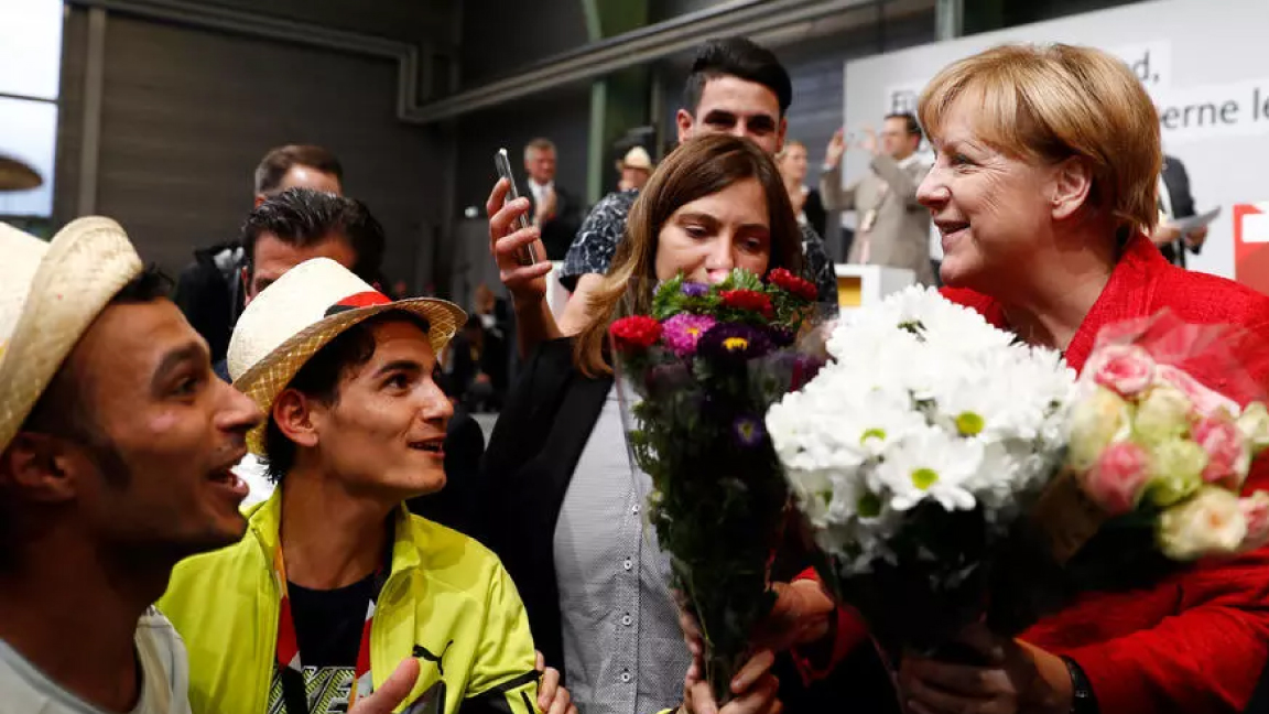 لاجئون سوريون يقدمون أزهارًا للمستشارة الألمانية أنغيلا ميركل في شمال ألمانيا في سبتمبر 2017