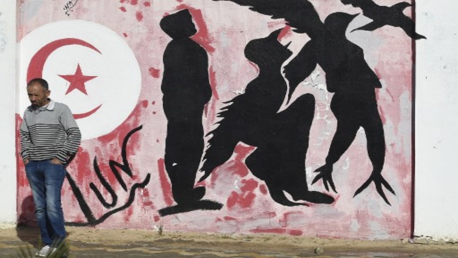 رجل ينتظر كتابات قرب جدران تصور صورة ظلية لرجل يتحول إلى طائر يرمز إلى الحرية ، في ساحة محمد البوعزيزي وسط مدينة سيدي بوزيد وسط تونس يوم 27 أكتوبر 2020 ، مهد الثورة التونسية 2011 حيث لا تزال البطالة قائمة