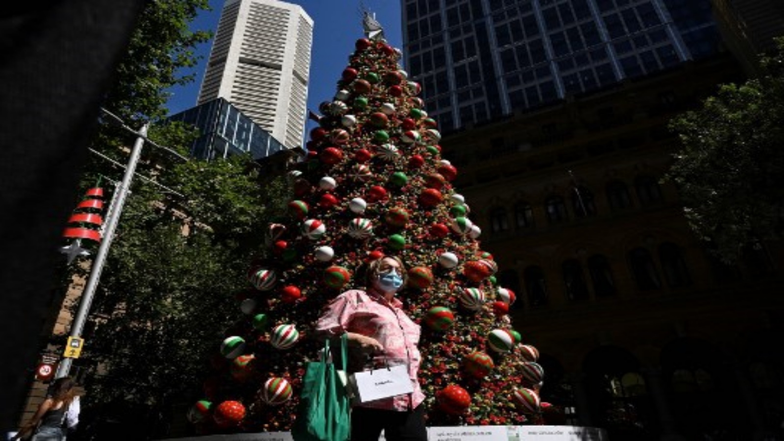 امرأة ترتدي قناعًا للوجه بسبب جائحة COVID-19 تمر عبر شجرة عيد الميلاد في Martin Place ، عادة ما تكون مليئة بالسياح ، في الحي التجاري المركزي في سيدني في 24 ديسمبر 2020.