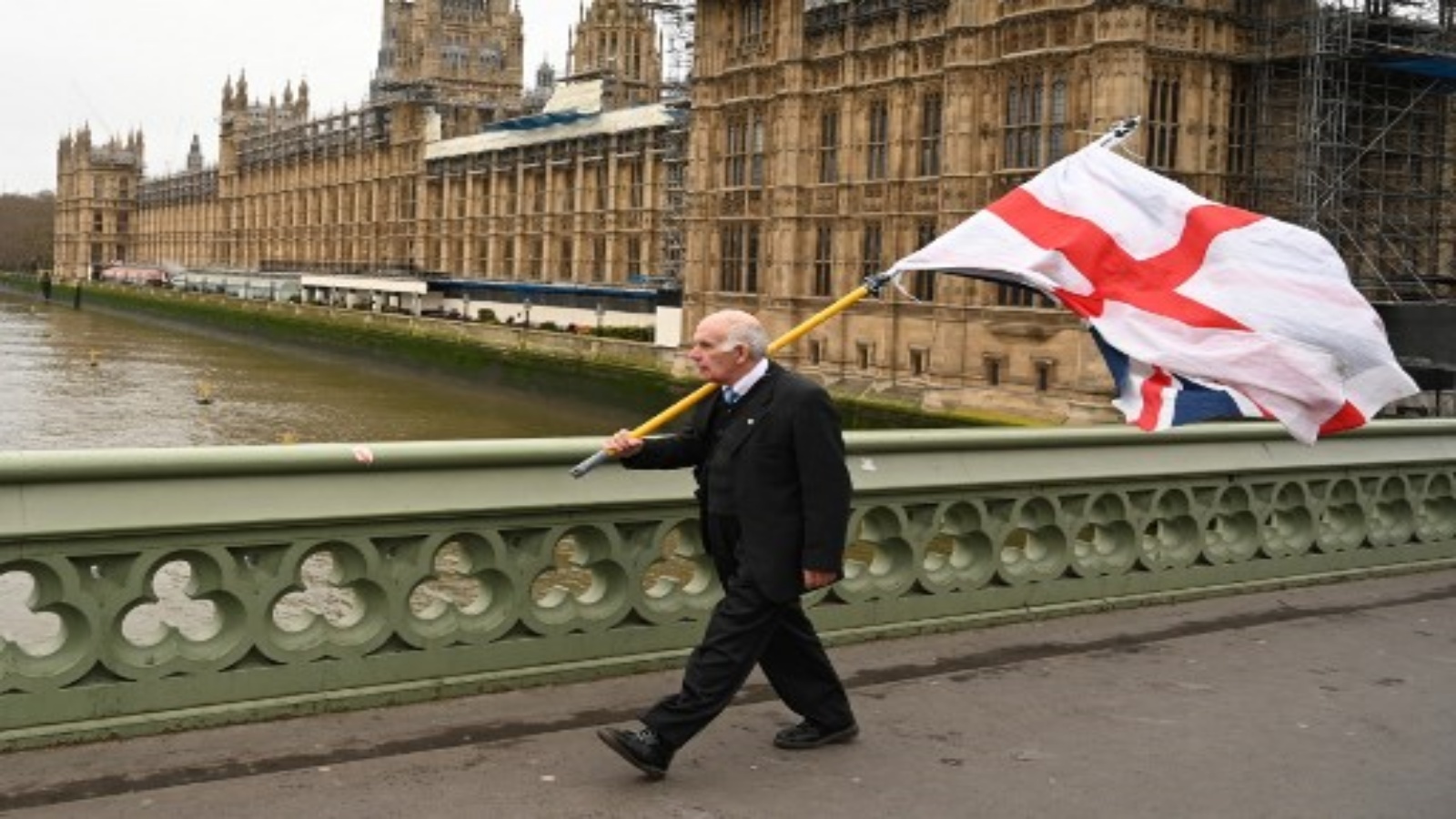 رجل يحمل علم سانت جورج ، العلم الوطني الإنجليزي ، إلى جانب علم الاتحاد وهو يسير على طول جسر وستمنستر بجوار مجلسي البرلمان في لندن