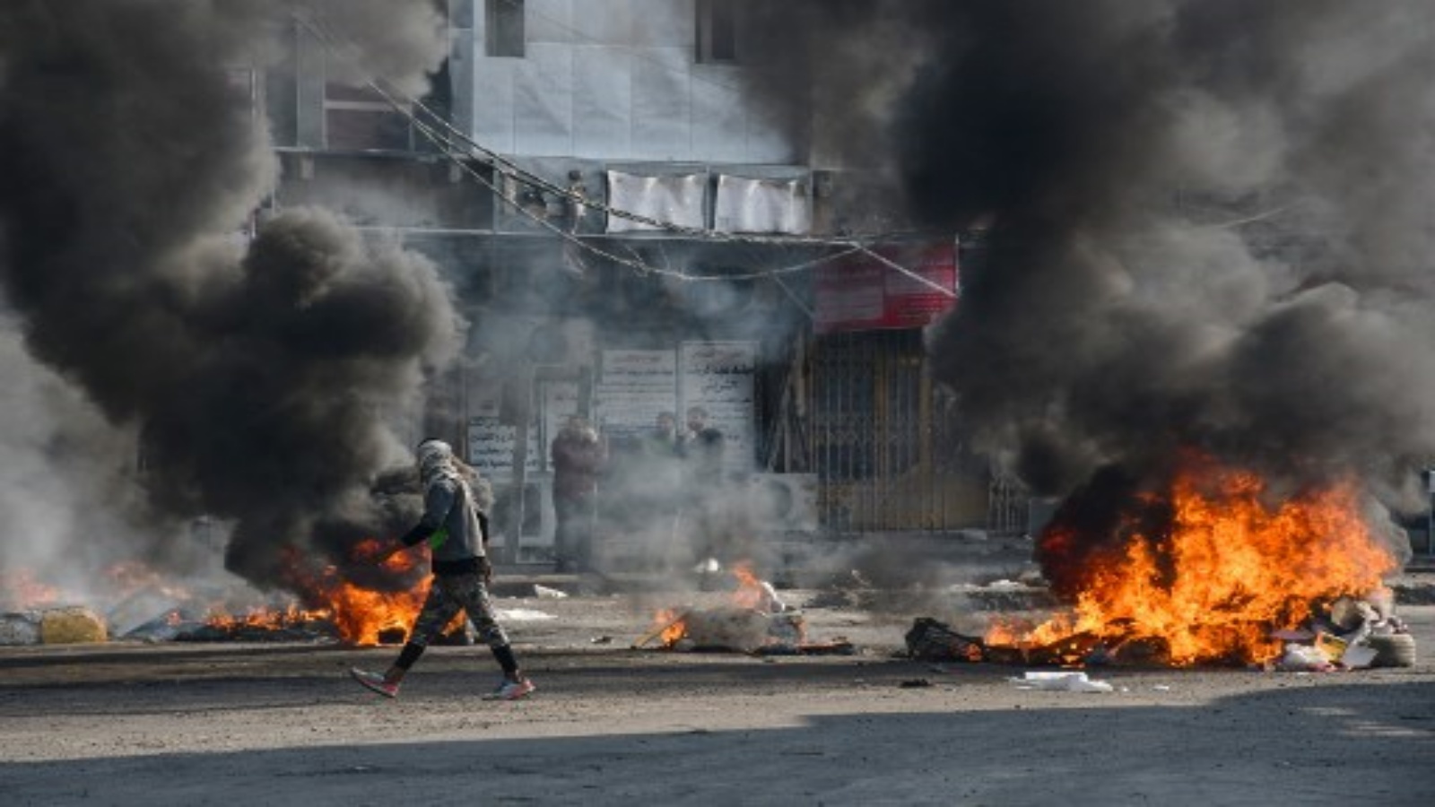 متظاهر عراقي يمر بجوار الإطارات المحترقة خلال اشتباكات مع الشرطة خلال مظاهرات مناهضة للحكومة في مدينة الناصرية بمحافظة ذي قار جنوبي العراق في 10 يناير 2021.