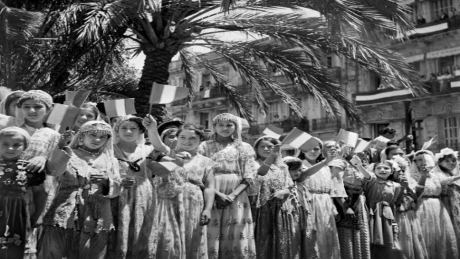 صورة التقطت في 1 يونيو 1949 فتيات جزائريات يرتدين فساتين تقليدية يلوحن بالأعلام الفرنسية خلال احتفال عام في الجزائر العاصمة.