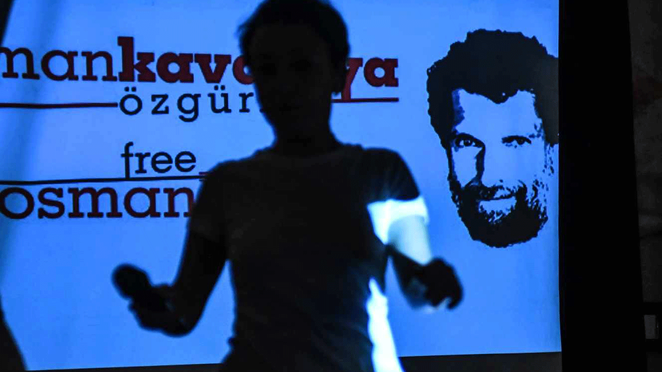 رجل يمر أمام صورة عثمان كافالا تظهر على شاشة خلال مؤتمر صحافي عقده المحامون المدافعون عنه في اسطنبول في 31 تشرين الأول/أكتوبر 2018