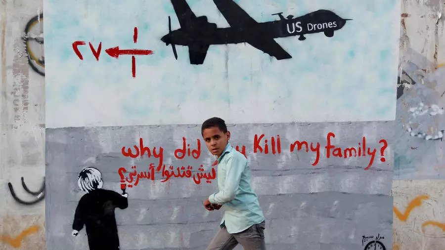 طفل يمني يقف أمام جدارية منددة بغارات المسيرات الأميركية في اليمن