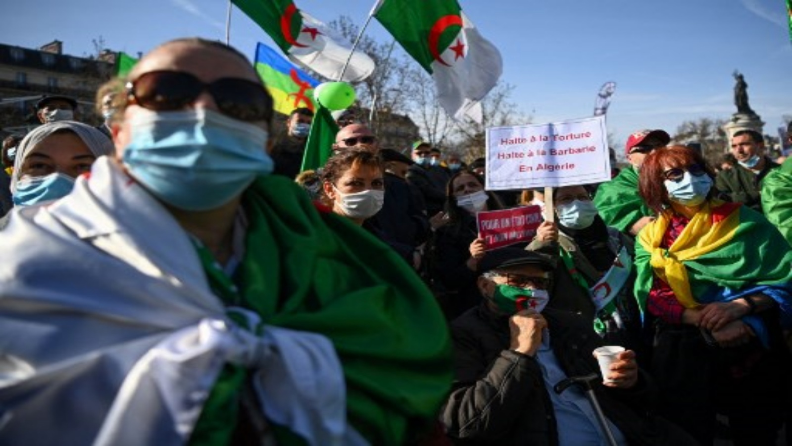 متظاهرون يحملون لافتة كتب عليها `` أوقفوا التعذيب وأوقفوا البربرية في الجزائر '' ويلوحون بالأعلام الوطنية الجزائرية خلال مسيرة في باريس في 21 فبراير 2021 ، دعما لحركة الحراك المناهضة للحكومة في الجزائر