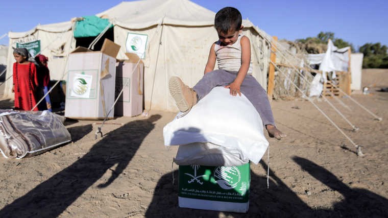طفل يمني يجلس على صناديق مساعدات سعودية