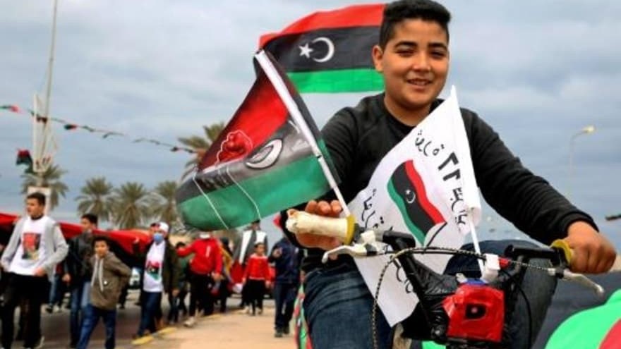 شاب ليبي على دراجة يحمل أعلاما وطنية في العاصمة طرابلس بتاريخ 25 شباط/فبراير 2021 في الذكرى العاشرة لثورة 2011 التي أسقطت نظام معمر القذافي