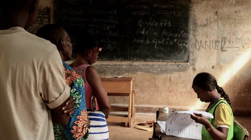 ينتظر الناخبون بينما تقوم مسؤولة في اللجنة الانتخابية بفحص قائمة الناخبين في مركز الاقتراع في بانغي بجمهورية أفريقيا الوسطى الأحد أثناء الانتخابات التشريعية في البلاد.