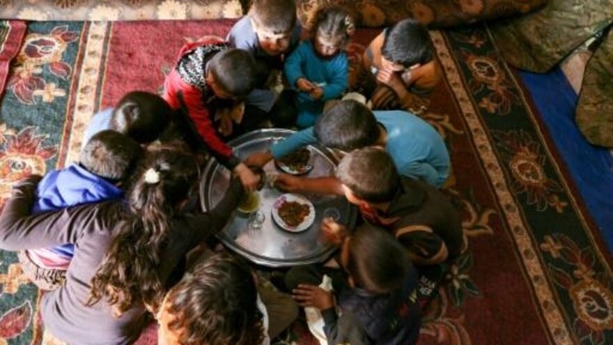  أحفاد عبد الرزاق خاتون يفترشون الأرض داخل خيمة لتناول الطعام في 11 آذار/مارس 2021 في قرية حربنوش في محافظة إدلب في شمال غرب سوريا
