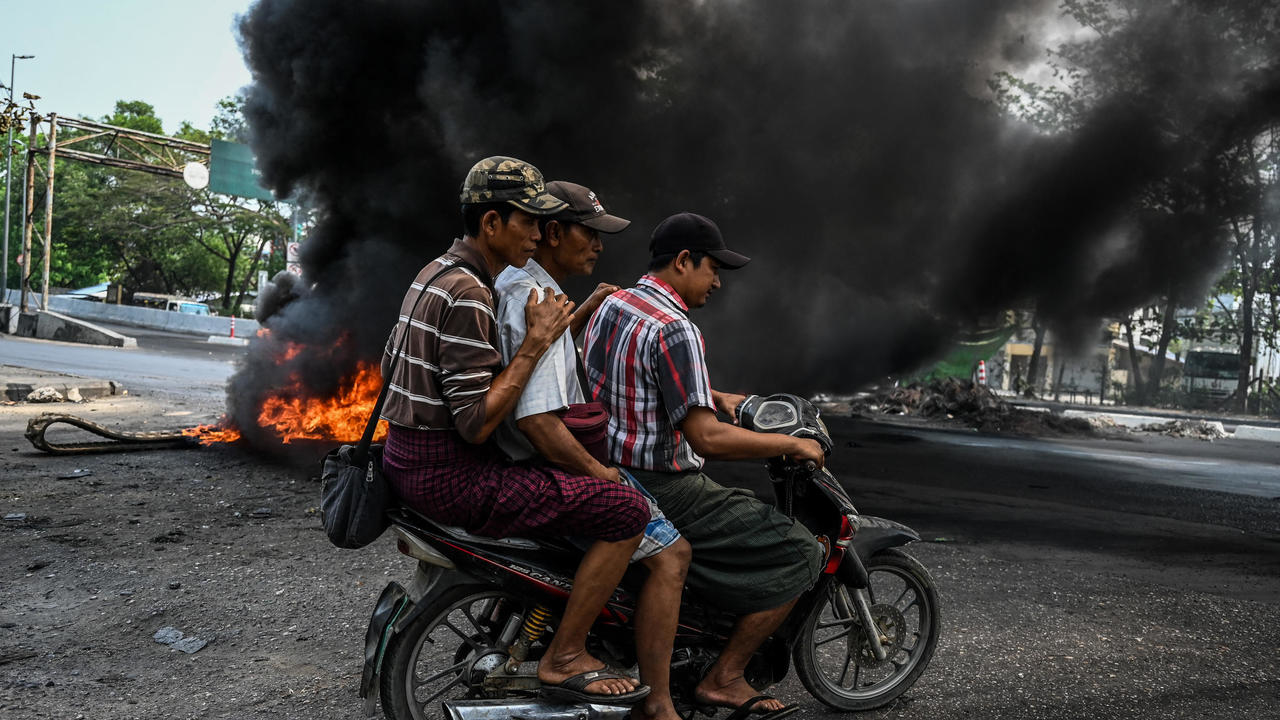 رجال على متن دراجة بخارية يمرون أمام حاجز محترق في رانغون في بروما في 17 آذار/مارس 2021