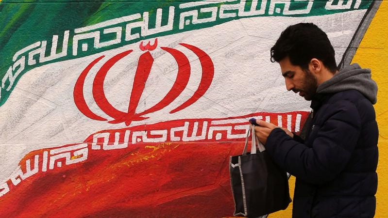 شاب يمر أمام رسم جداري للعلم الإيراني في طهران