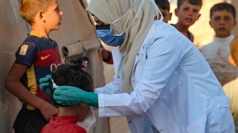 عاملة في القطاع الصحي تساعد طفل على وضع الكمامة في احدى المخيمات في إدلب