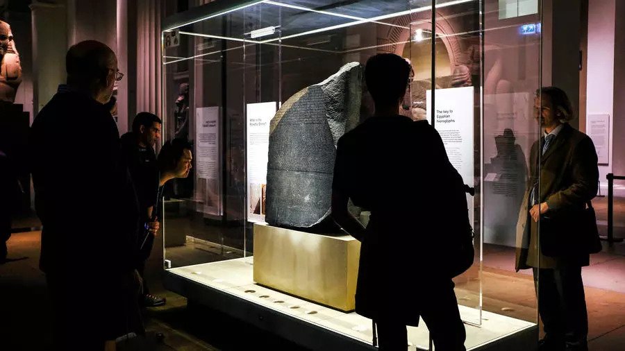 زوار في المتحف البريطاني في لندن في 13 تشرين الثاني/نوفمبر 2018 يتأملون حجر رشيد الذي اكتشفه جنود فرنسيون في ممفيس في مصر في 1799 وسمح بفك شيفرة اللغة الهيروغليفية ونشأة علم المصريات