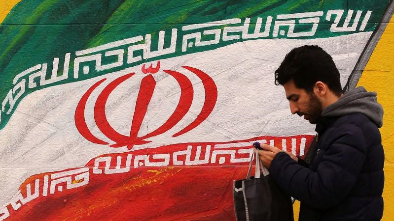 إيراني يمر بجدارية تمثل علم بلاده في أحد شوارع طهران