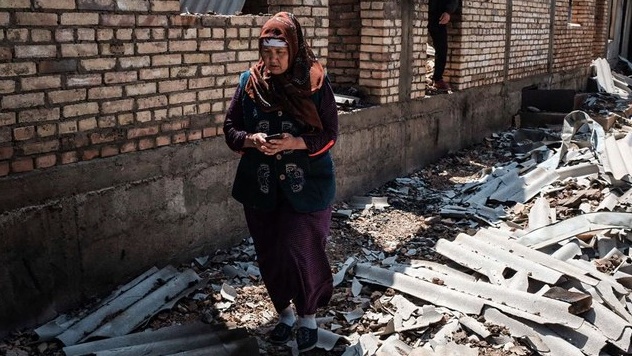 سيدة قرغيزستانية تقف أمام منزلها المدمر
