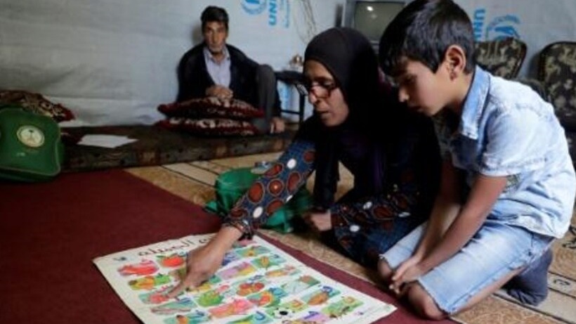 الطفل السوري اللاجئ محمد (11 عاماً) يجلس قرب والدته التي تتولى تعليمه الأحرف العربية على ملصق 