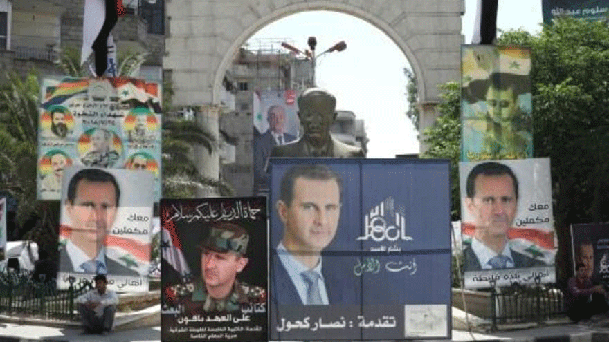 رجل يجلس بجوار تمثال للرئيس السوري السابق حافظ الأسد محاطا بملصقات انتخابية لنجله الرئيس السوري بشار الأسد في دمشق في 23 أيار/مايو 2021