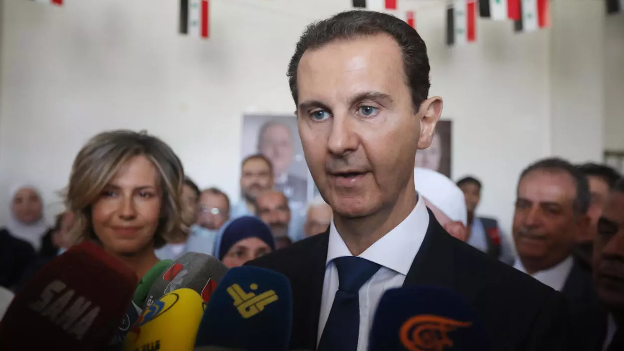 الأسد متحدث الى الاعلام وتظهر زوجته في الخلفية