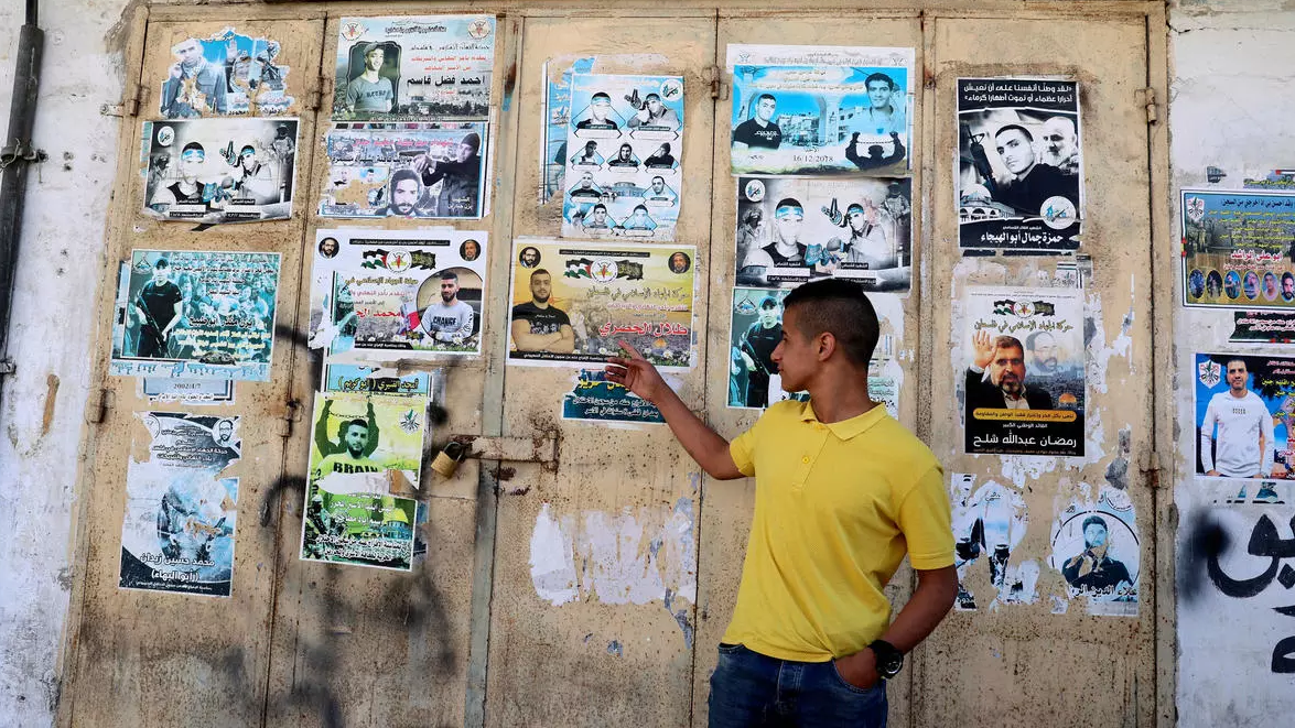 الفتى الفلسطيني أشرف أحمد (17 عاما) يقف أمام جدار الصقت عليه صور 