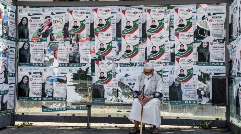 رجل مسن يجلس في محطة حافلات مغطاة بلافتات انتخابية لمرشحة 