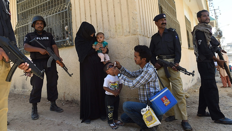 رجال شرطة باكستانيون يقفون في حراسة بينما يقوم عامل صحي بتطعيم طفل خلال حملة التطعيم ضد شلل الأطفال 