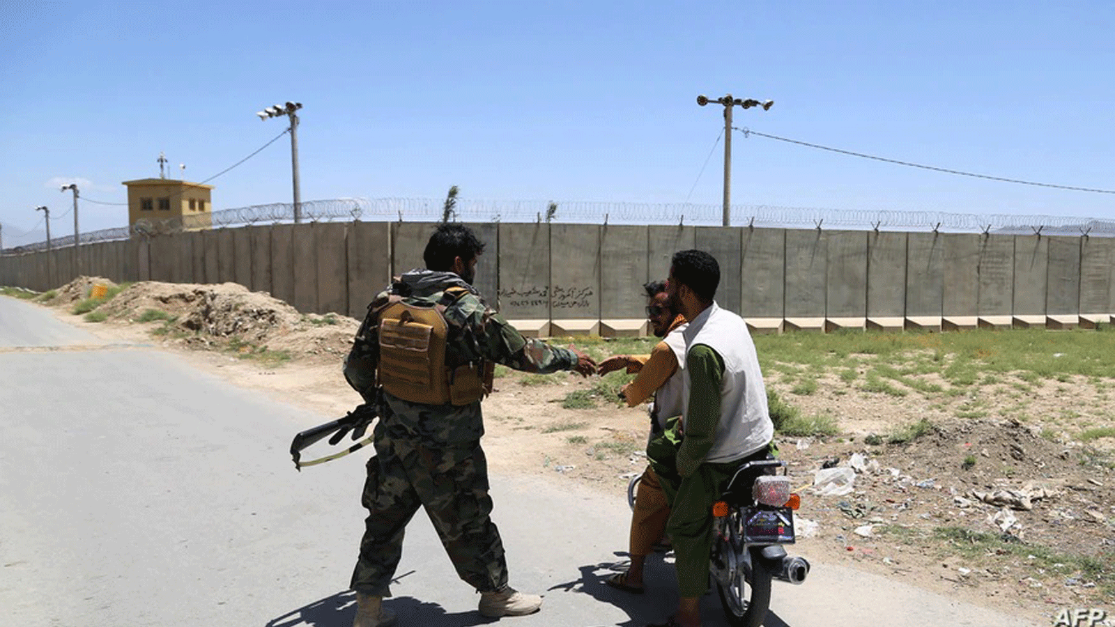 جندي من الجيش الوطني الأفغاني (ANA) يحيي السكان المحليين الذين يركبون دراجة نارية خارج قاعدة باغرام الجوية، بعد انسحاب كل قوات الولايات المتحدة وحلف شمال الأطلسي على بعد حوالي 70 كيلومترًا شمال كابول في 2 تموز/يوليو 2021.