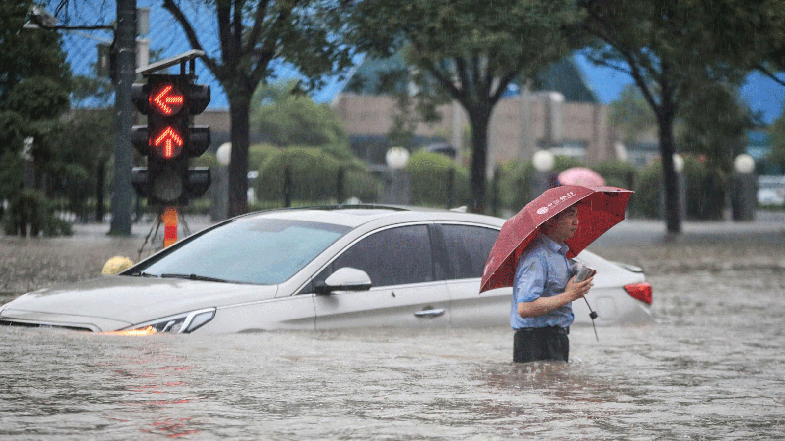 رجلٌ يمر أمام سيارة غارقة في شارع غمرته المياه بعد هطول أمطار غزيرة في مدينة تشنغتشو في الصين. 20 تموز/يوليو 2021