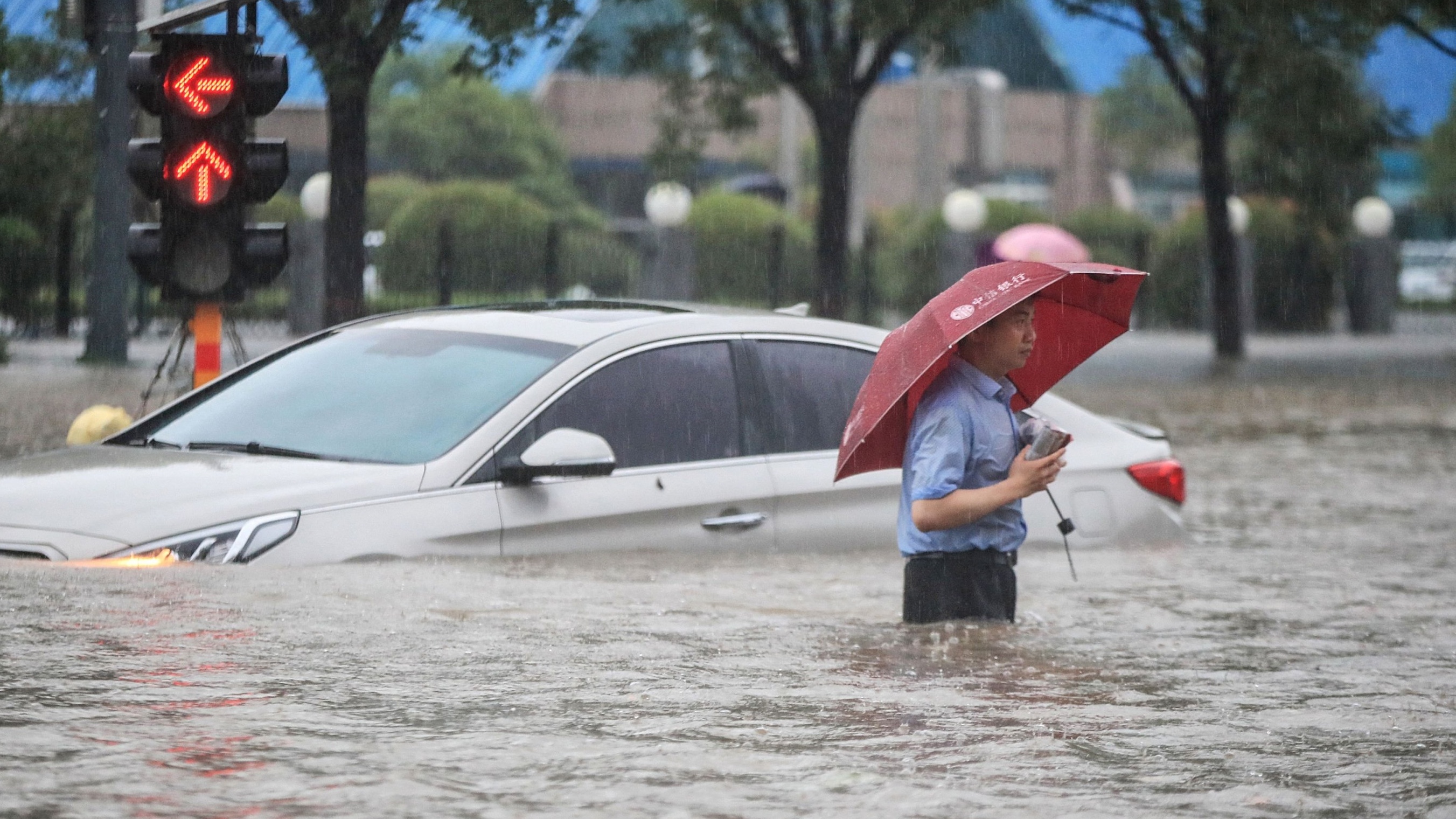 رجل يحاول عبور الطريق وبجانبه سيارته العالقة وسط المياه في مدينة تشنغتشو في الصين بتاريخ 21 تموز/يوليو 2021