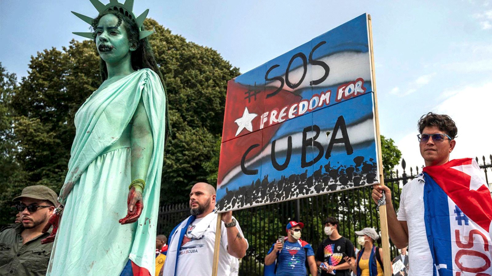 متظاهر يرتدي زي تمثال الحرية بينما يرتدي آخرون الأعلام الكوبية خلال مظاهرة أمام البيت الأبيض في واشنطن العاصمة، في 25 تموز/يوليو 2021.