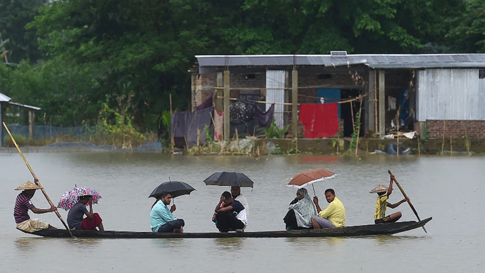  أشخاص يركبون قاربًا عبر المياه في أراضي غمرتها الفيضانات في سونامجونغ، بنغلاديش، 14 تموز/يوليو 2020