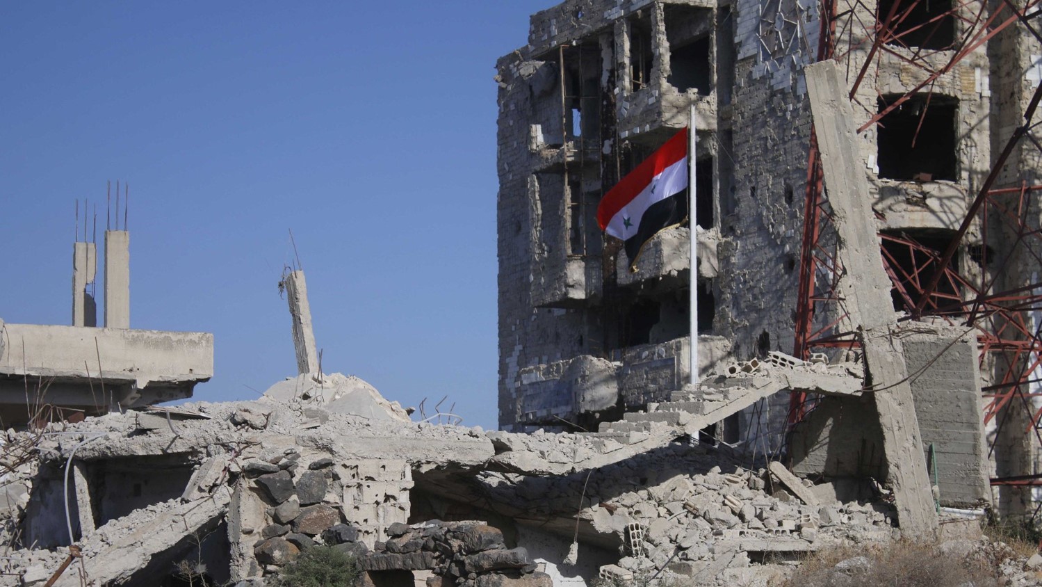 علم النظام السوري فوق أنقاض مبنى مدمر في درعا