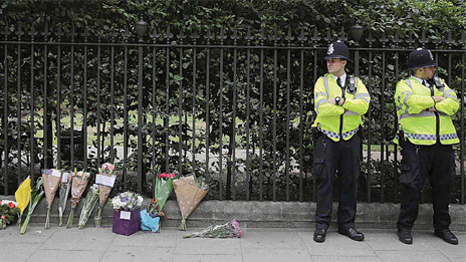 أفراد من الشرطة بجوار الأزهار التي وضعها الناس كتحية لأرواح الضحايا في ميدان راسل بلندن، بتاريخ 3 آب/أغسطس 2016، بعد موجة طعن أدت إلى مقتل امرأة وإصابة خمسة آخرين.