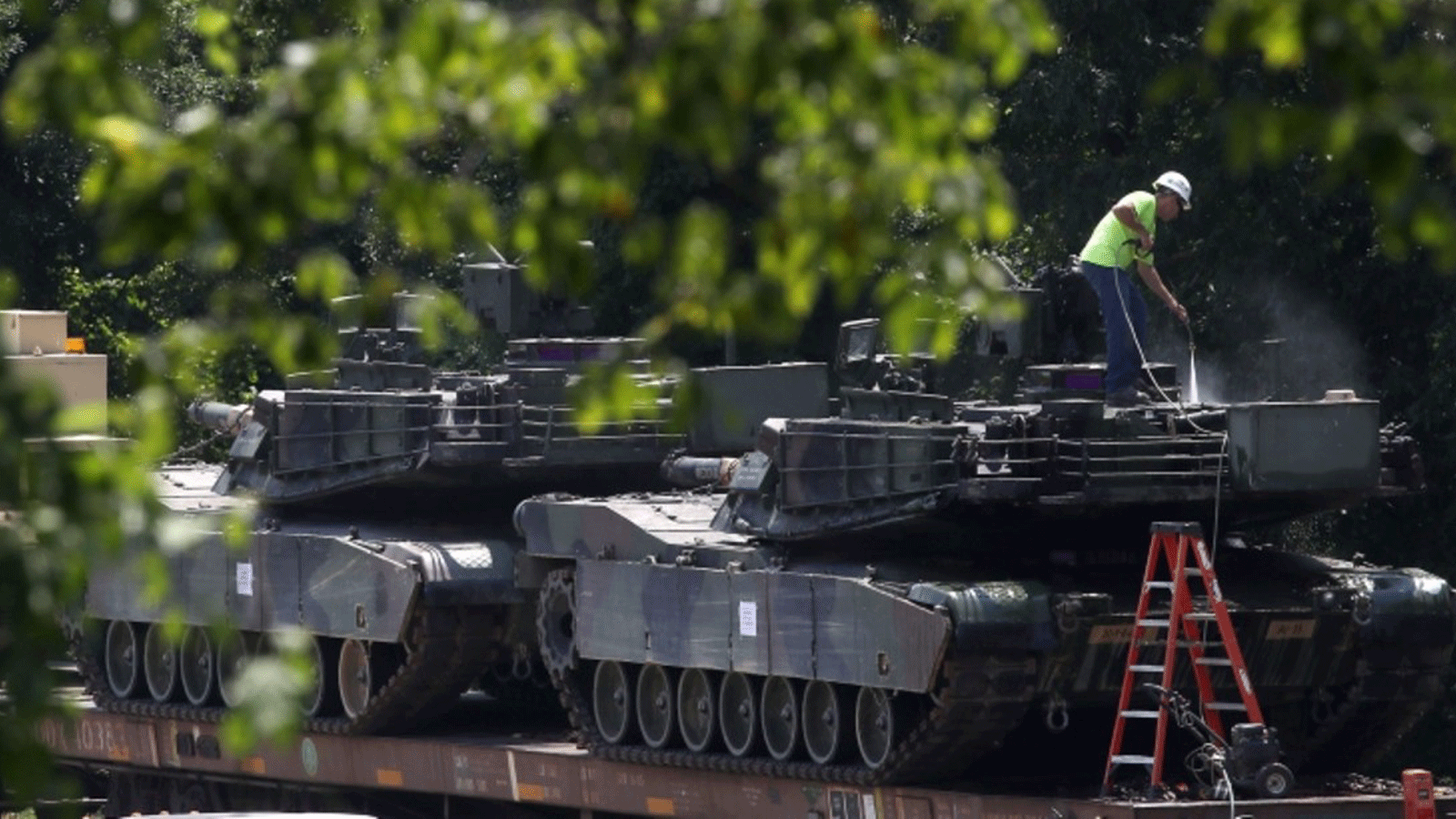 عامل يغسل دبابات M1A1 Abrams تم تحميلهما على عربات سكة حديد في ساحة للسكك الحديدية في 2 تموز/يوليو 2019 في واشنطن
