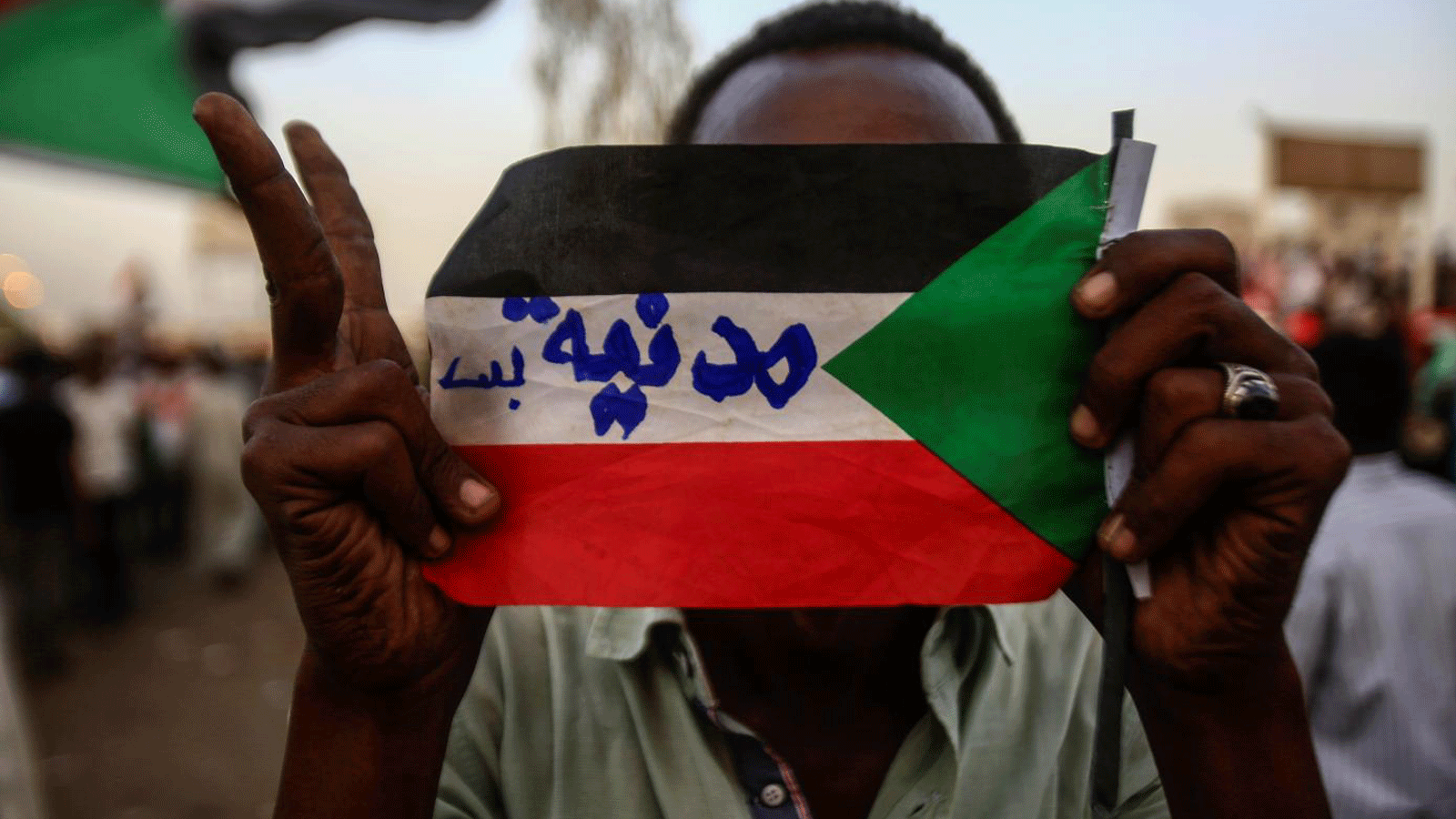 متظاهر سوداني يحمل العلم الوطني وكتاباته بالعربية 