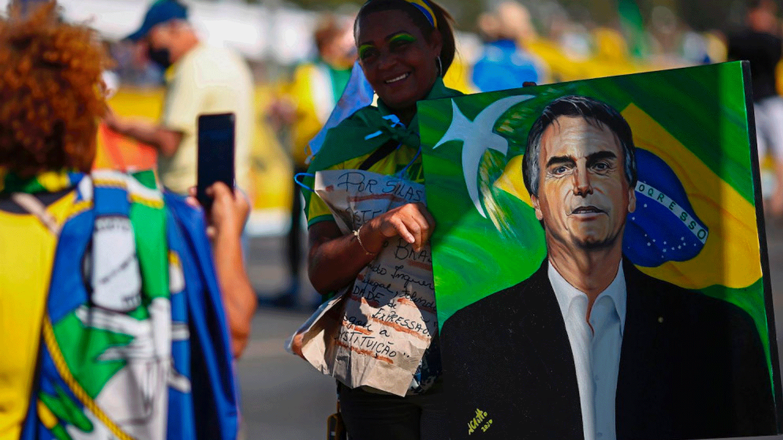امرأة تقف لالتقاط صورة سريعة وهي تحمل صورة الرئيس البرازيلي جاير بولسونارو خلال مظاهرة لدعمه في برازيليا في 21 حزيران/يونيو 2021 