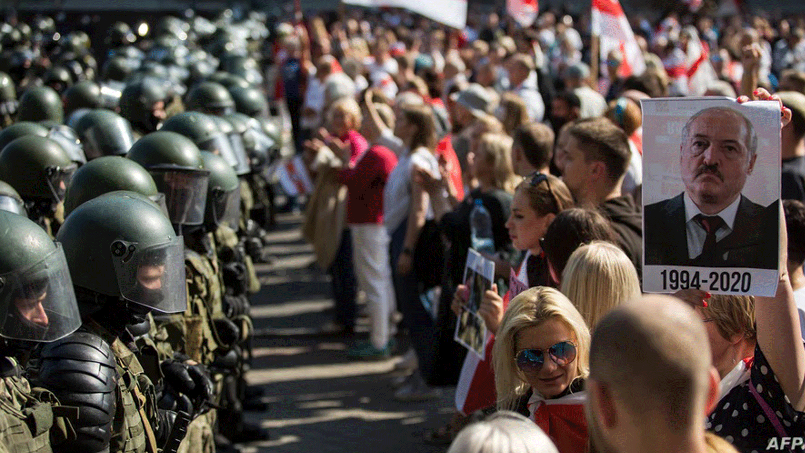 قوات الأمن البيلاروسية تُغلِق شارعًا خلال تجمع معارض يطعن في نتائج الانتخابات الرئاسية الرسمية. في مينسك، بيلاروسيا، 30 آب/أغسطس 2020. ويظهر على اللافتة رسم الرئيس ألكسندر لوكاشينكو والسنوات التي قضاها في السلطة.