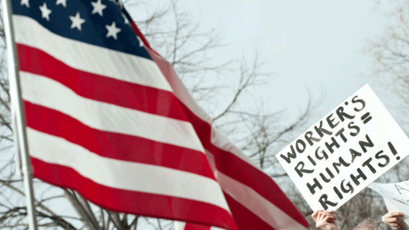 لافتة تربط حقوق العمال بحقوق الإنسان الى جانب العلم الأميركي في تظاهرة للعمال