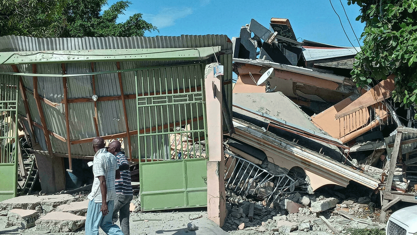 أشخاص يسيرون بالقرب من منزل منهار ضربه الزلزال في 14 آب/ أغسطس 2021 في ليس كاي ، جنوب غرب هايتي.